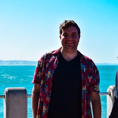 Matt smiling beside a bright blue sea, wearing a floral shirt